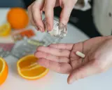 Dłoń z kapsułką, obok pomarańcze i cytryna. Pytanie: laktoferyna przed czy po jedzeniu?