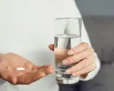 Dłoń z tabletką i szklanką wody. Czy l-treonian magnezu skutki uboczne są powodem do niepokoju?