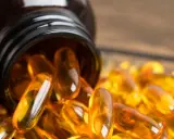 Bursztynowa butelka z kapsułkami omega 3 na serce rozsypanymi na drewnianym blacie.