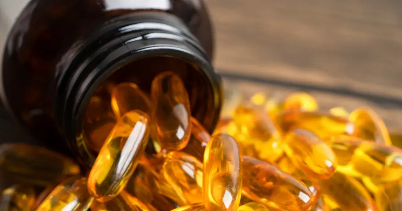 Bursztynowa butelka z kapsułkami omega 3 na serce rozsypanymi na drewnianym blacie.