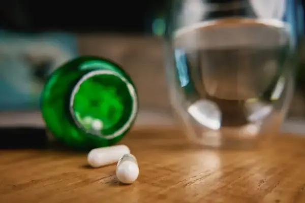 Berberyna a alkohol: dwie białe kapsułki obok zielonego opakowania i szklanki z wodą.